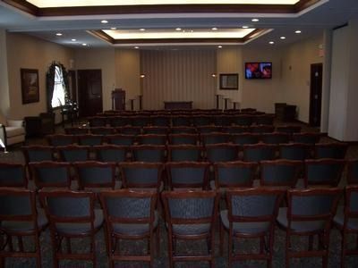 Rows of chairs face a stage in a formal room, possibly a chapel or auditorium.