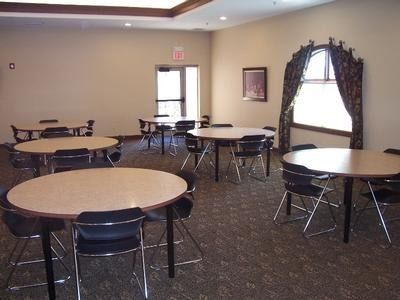 A room with round tables and chairs. Window with curtains on the right. An exit door is visible.