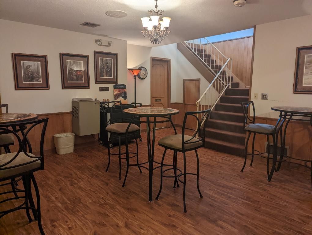 Bar area with high-top tables, chairs, and a staircase leading up. Artwork and a lamp decorate the walls.