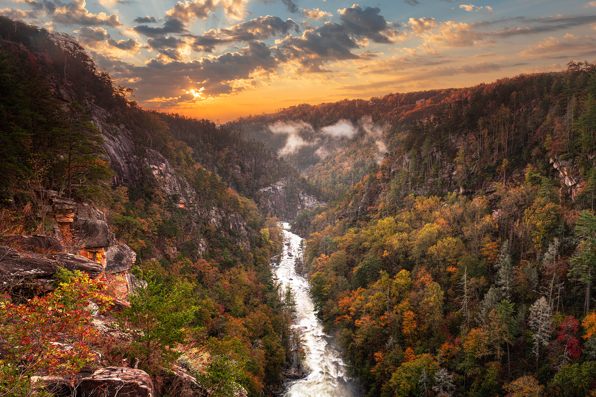 River cascades through a forested canyon at sunset, autumn colors in the trees, golden sky.