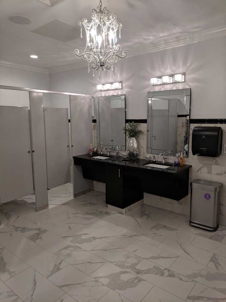 A modern public restroom with white marble tile, a dark vanity with two sinks, wall mirrors, and a chandelier.