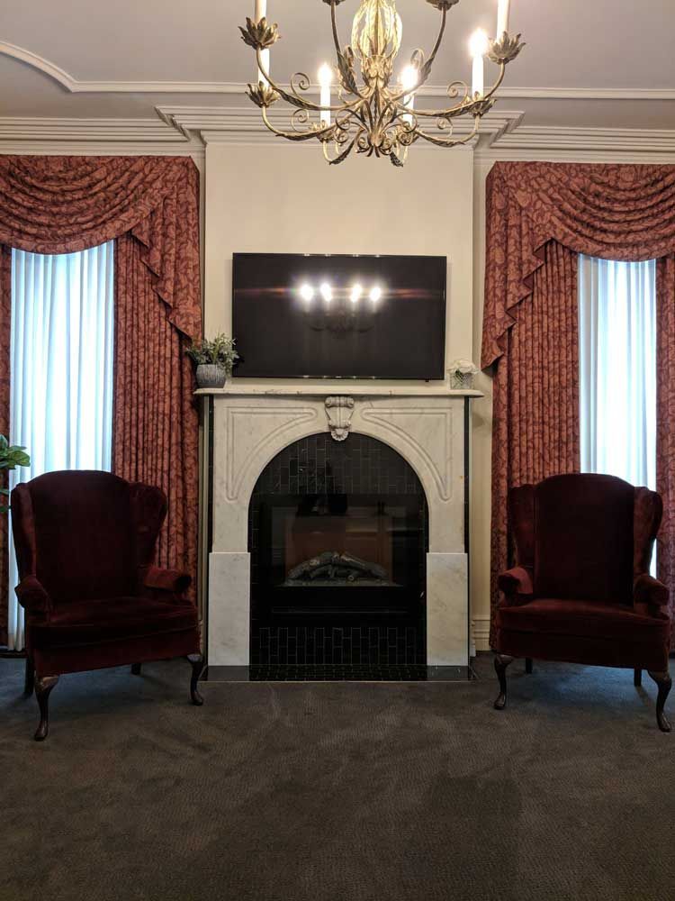 A living room features two maroon armchairs flanking an arched fireplace with a mounted television above it.