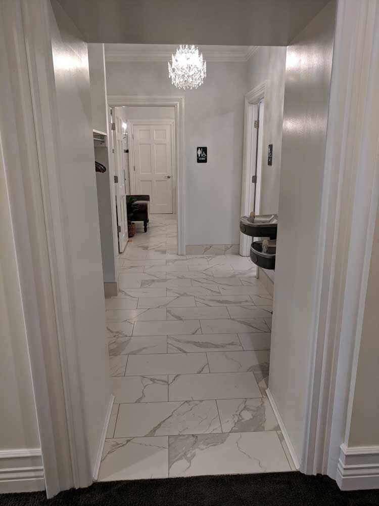 A view through a doorway into a marble-tiled hallway with a hanging light fixture and a sink on the right.