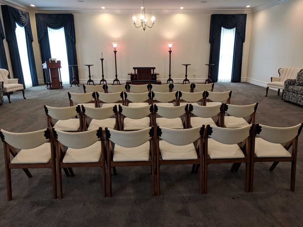 A spacious, formal room set up with rows of cream chairs facing a podium and altar, framed by dark blue curtains.