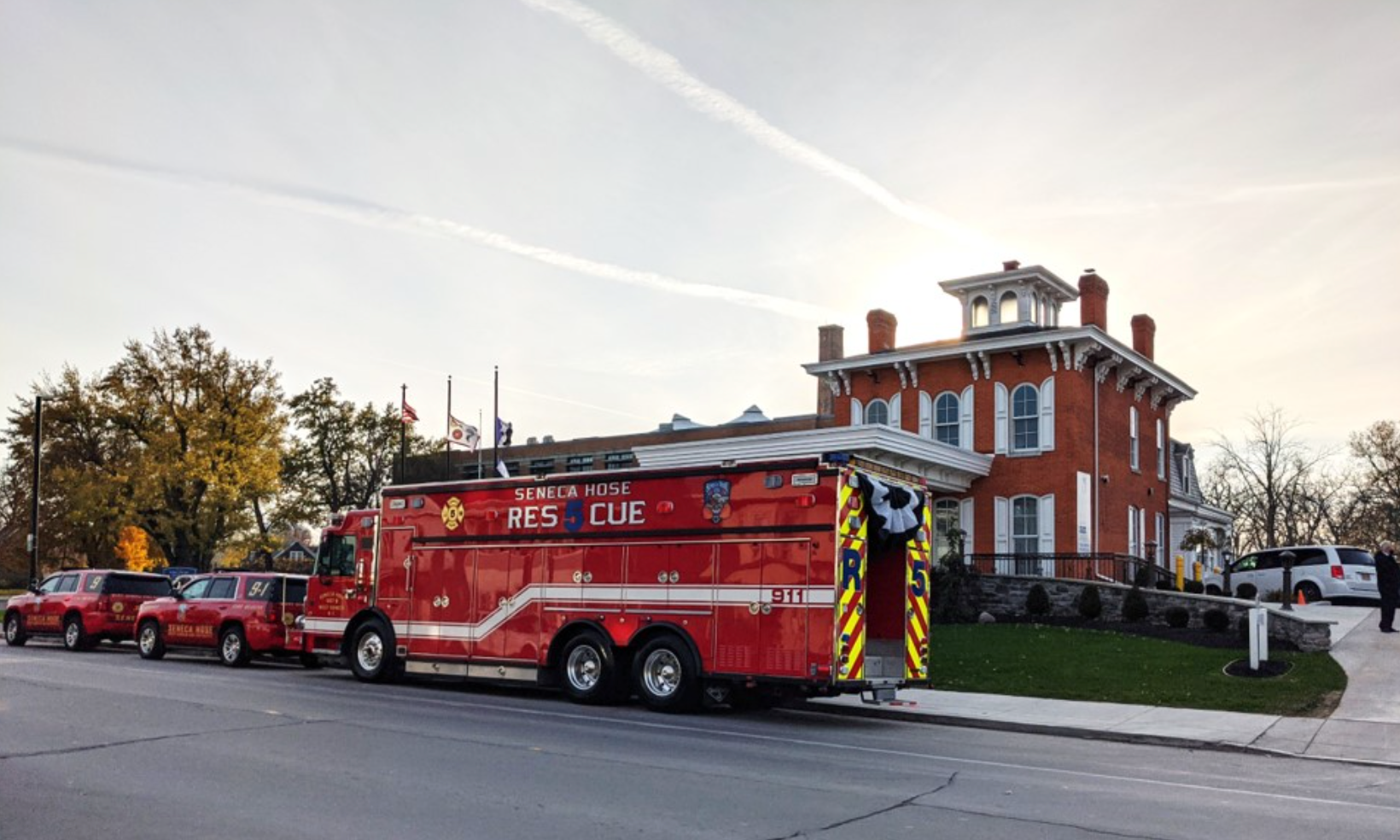 A red fire rescue truck parked on a street in front of a historic red brick house during the day.