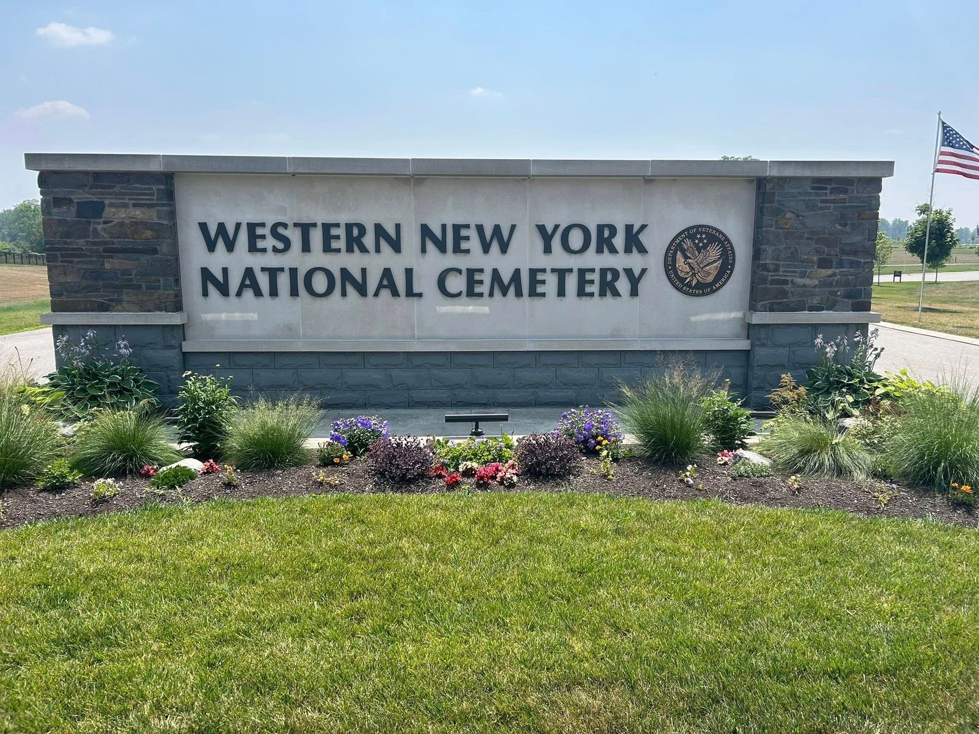 A stone sign for the Western New York National Cemetery with an American flag flying in the background.