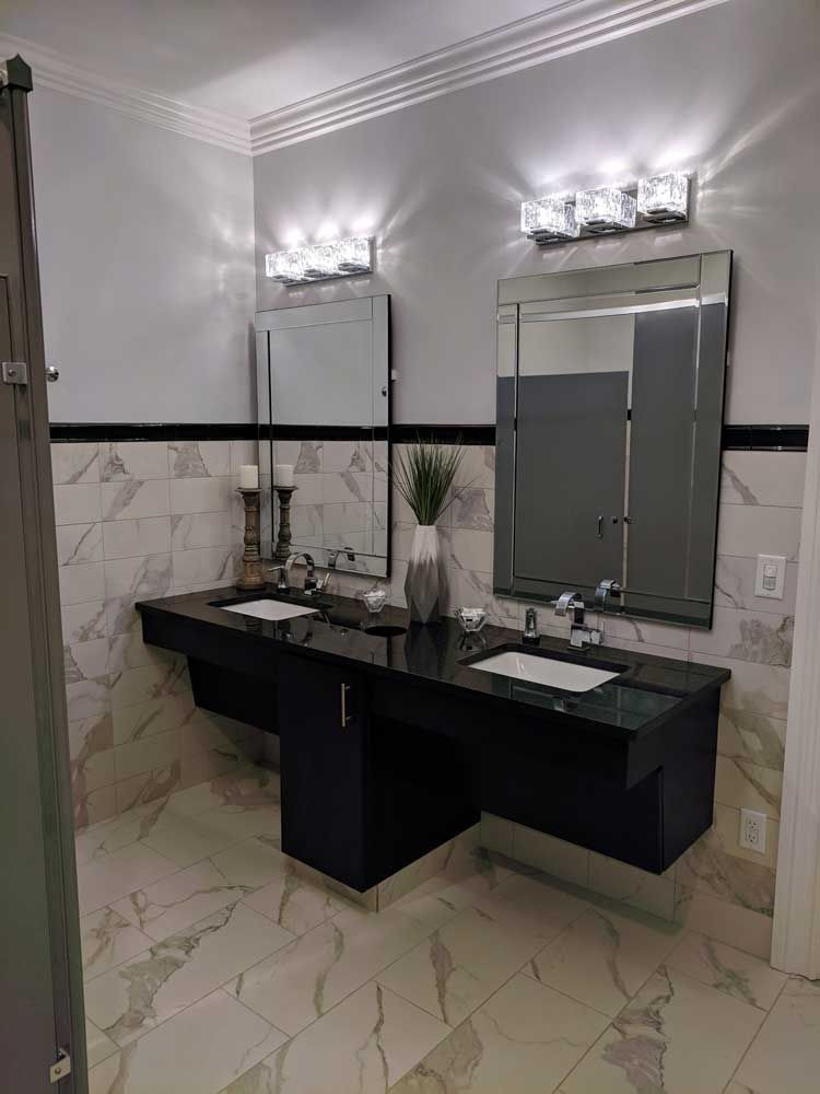 Modern double vanity with black countertops, two rectangular mirrors, wall-mounted light fixtures, and marble tiling.