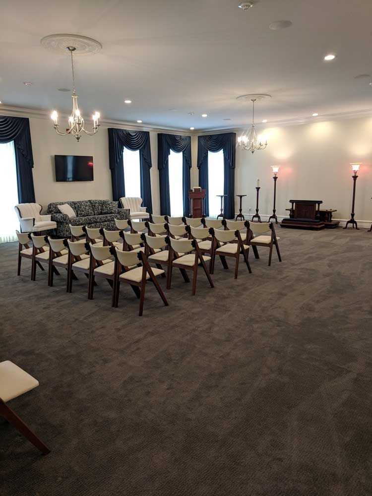 A spacious, carpeted room set up for a meeting with rows of wooden chairs, a couch in the back, and two chandeliers.