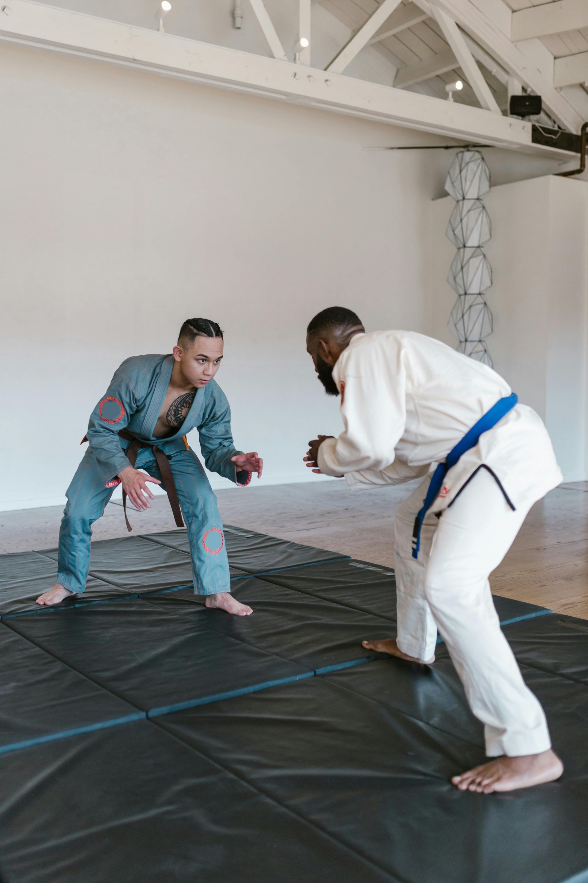 Two people in martial arts attire facing each other on a mat, preparing to spar.
