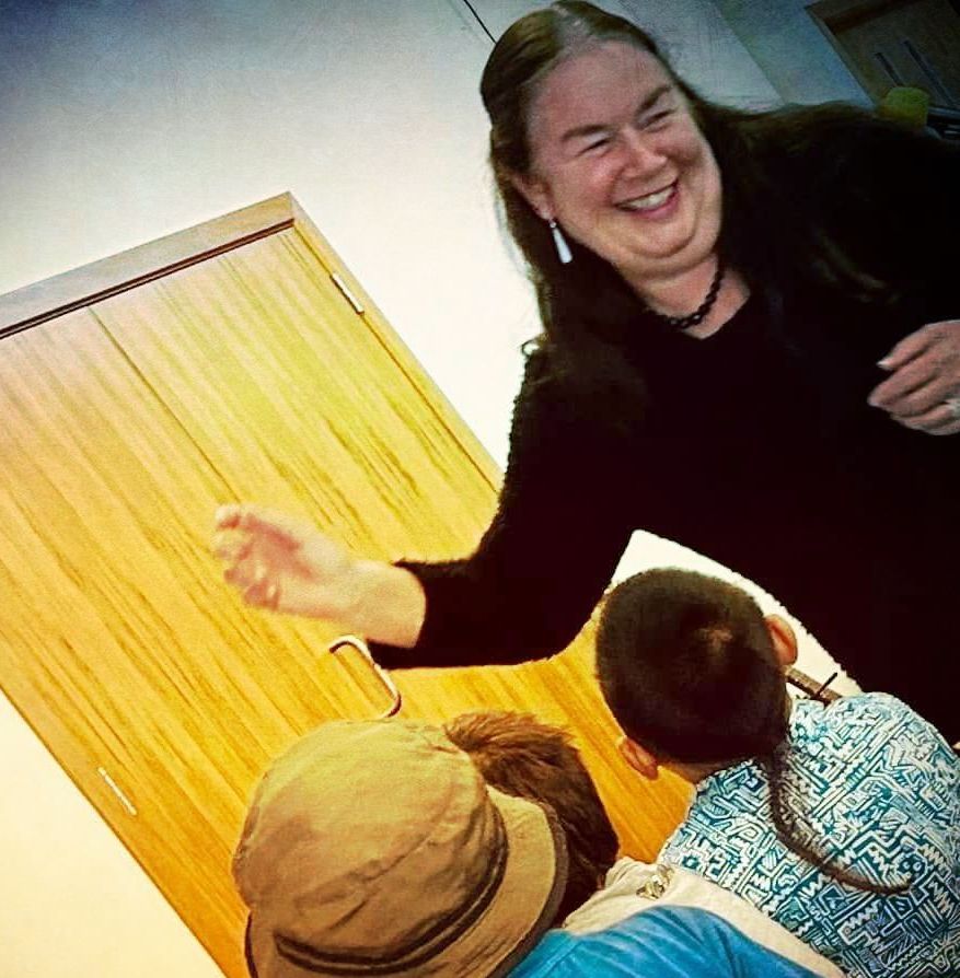 Woman laughing, reaching toward group of children near wooden door.
