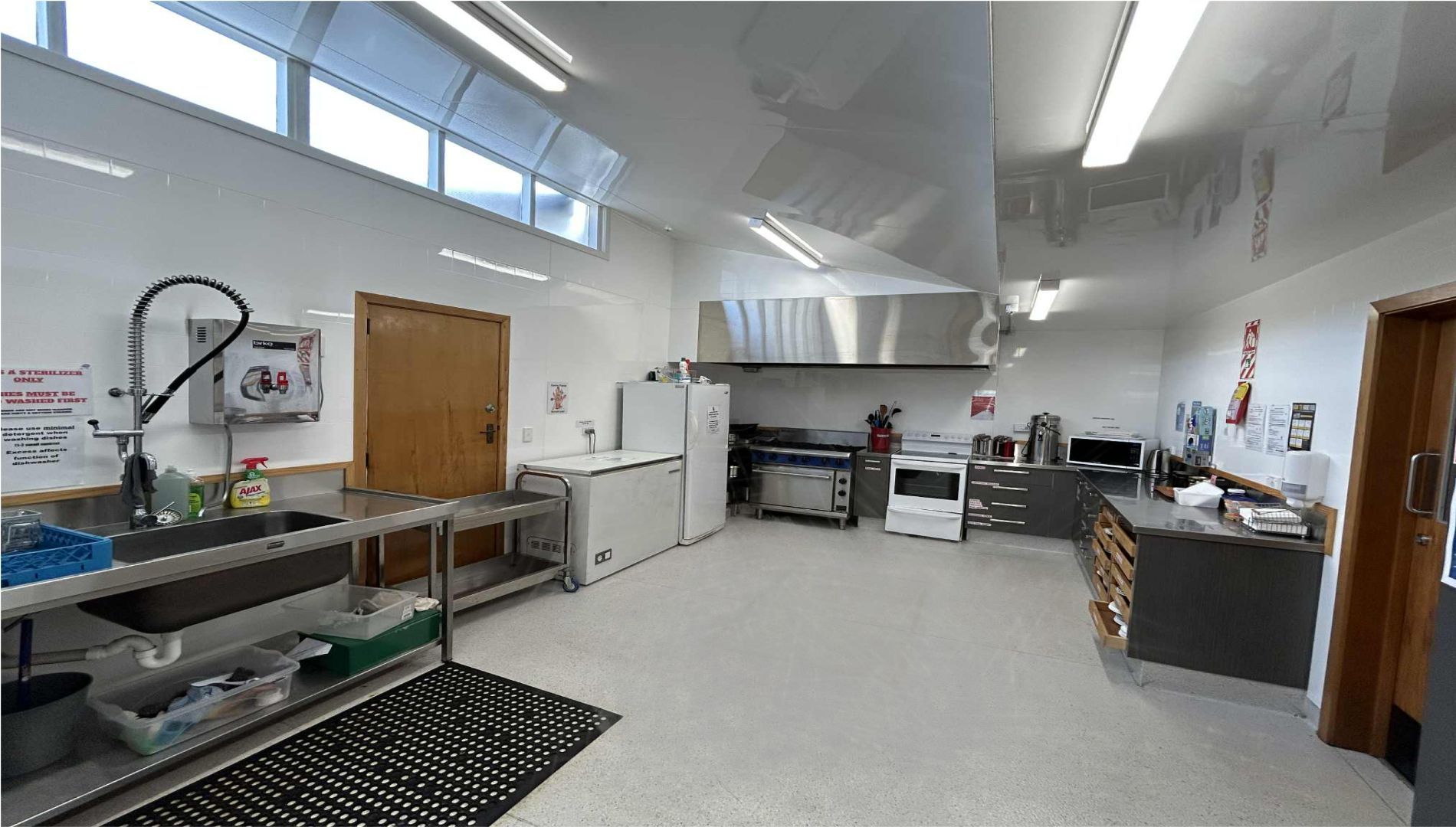 A commercial kitchen with stainless steel appliances, large windows, and work surfaces.  Linwood Venue 
