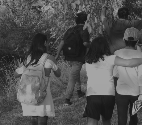 A group of children are walking through a field with their arms around each other