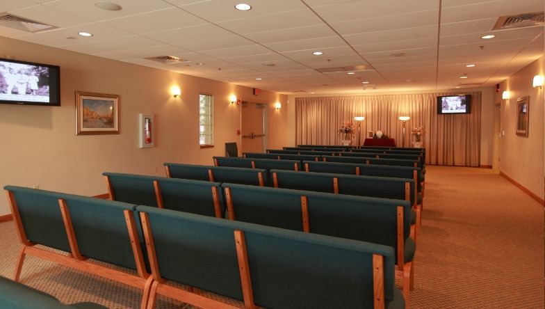 a funeral home with rows of green chairs and a television on the wall .