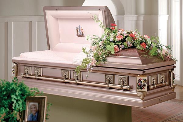 a pink coffin with flowers on top of it is sitting on a table next to a picture of a man .