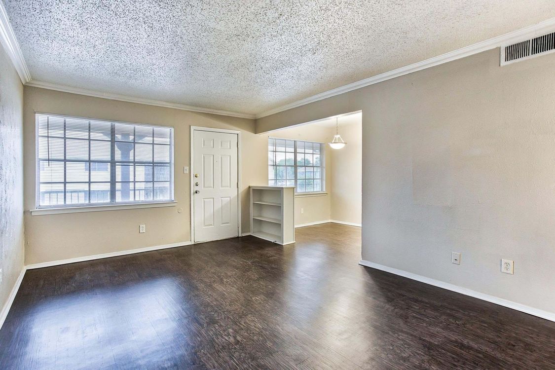 An empty living room with hardwood floors and a white door at Senita Apartment Homes in Dallas, TX!