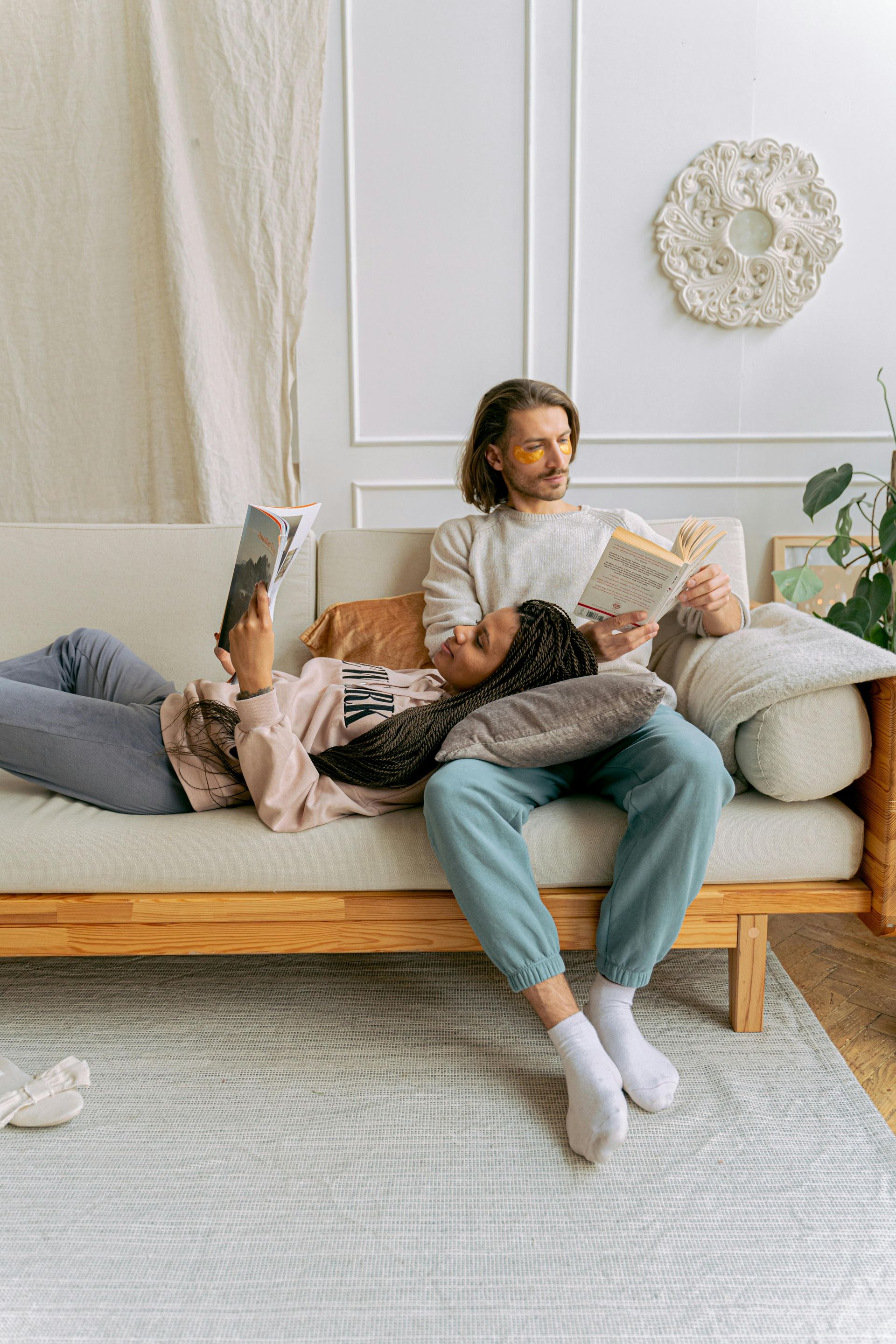 A man and a woman are sitting on a couch reading books.