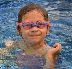 child wearing pink and purple swimming goggles while in the water.
