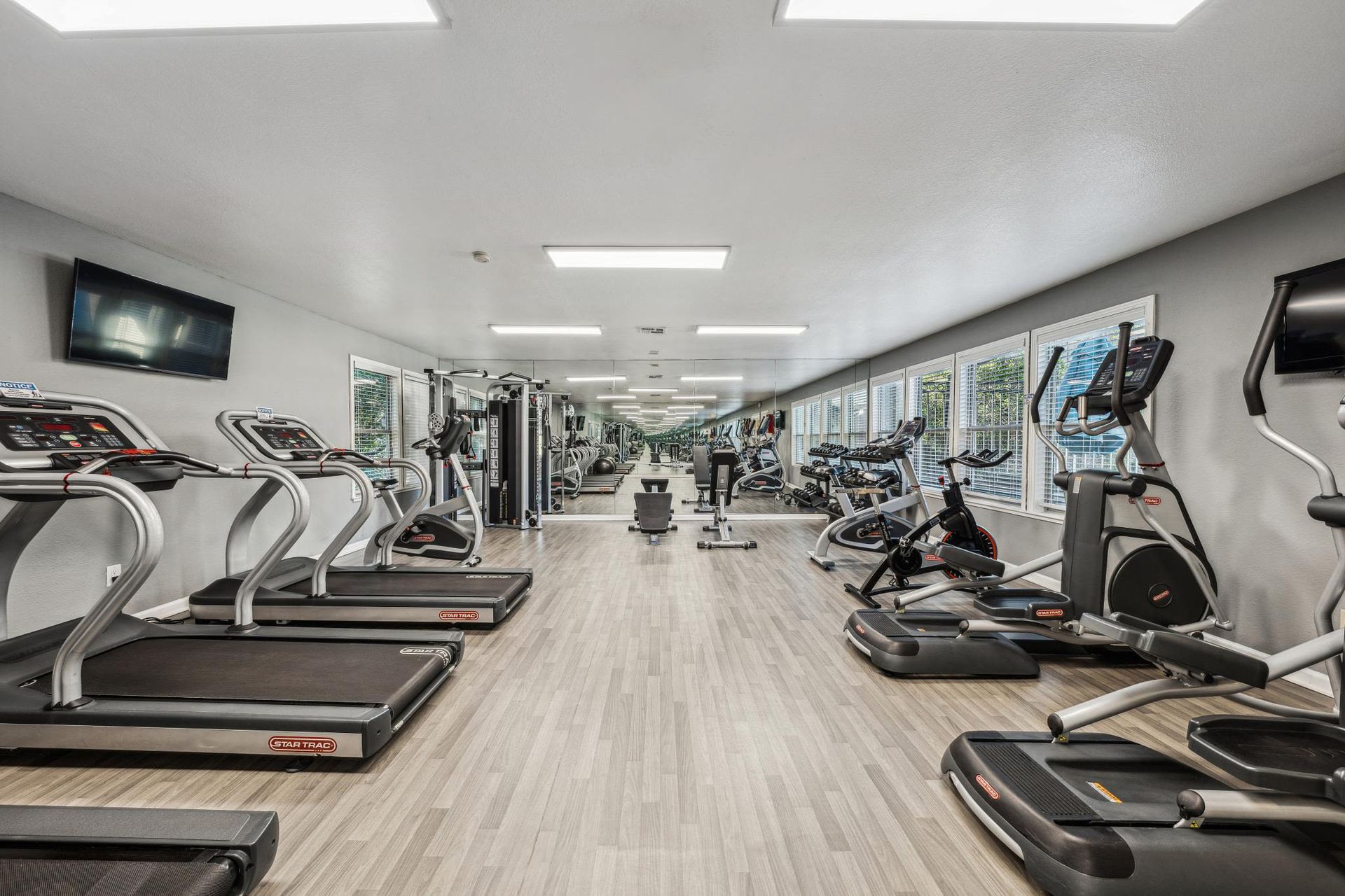 Well-lit fitness center with treadmills, bikes, and weight machines along large windows.