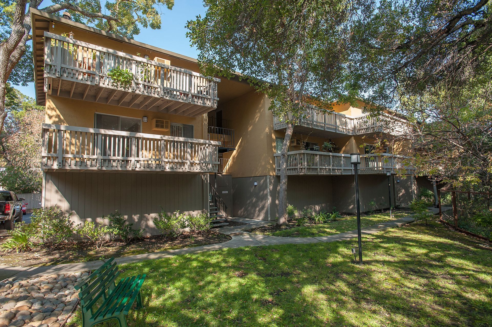 Exterior view of a beige, multi-unit building with wooden balconies and surrounding trees.