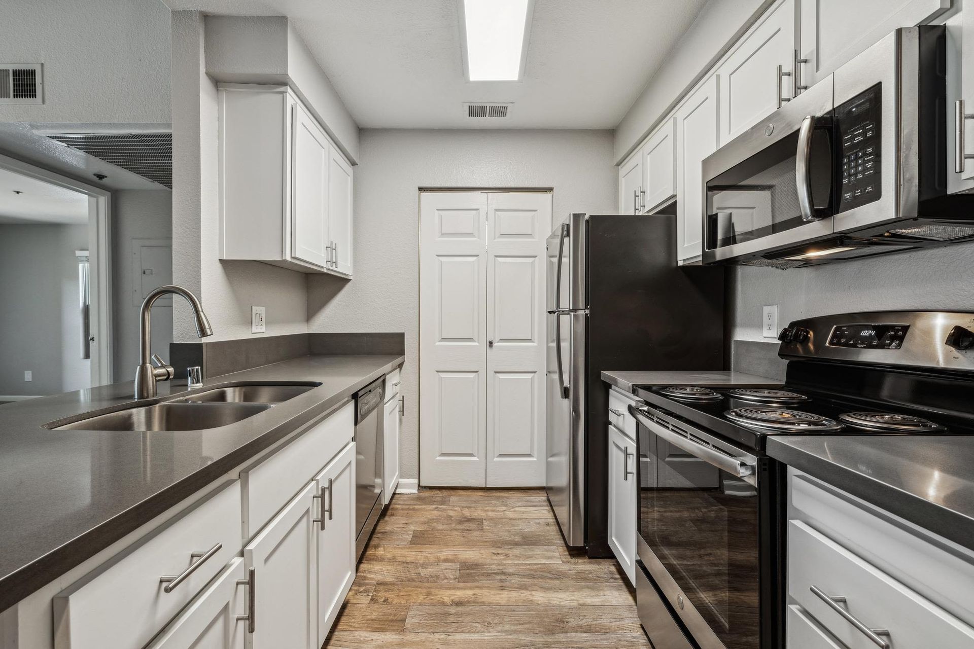 Modern apartment kitchen with stainless steel appliances, white cabinets, and gray countertops.
