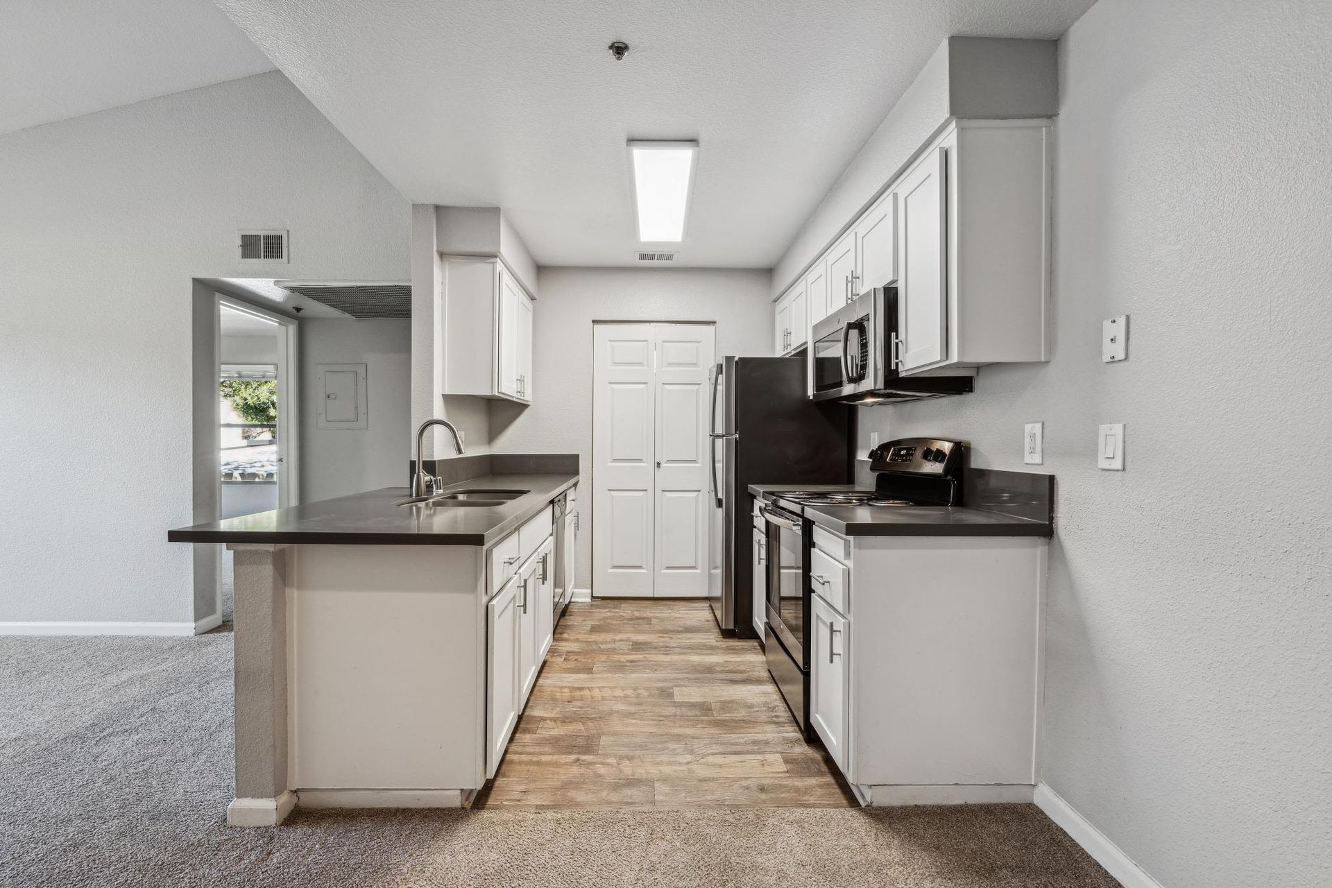 Interior apartment kitchen with white cabinets, dark countertops, an island, and stainless steel appliances.
