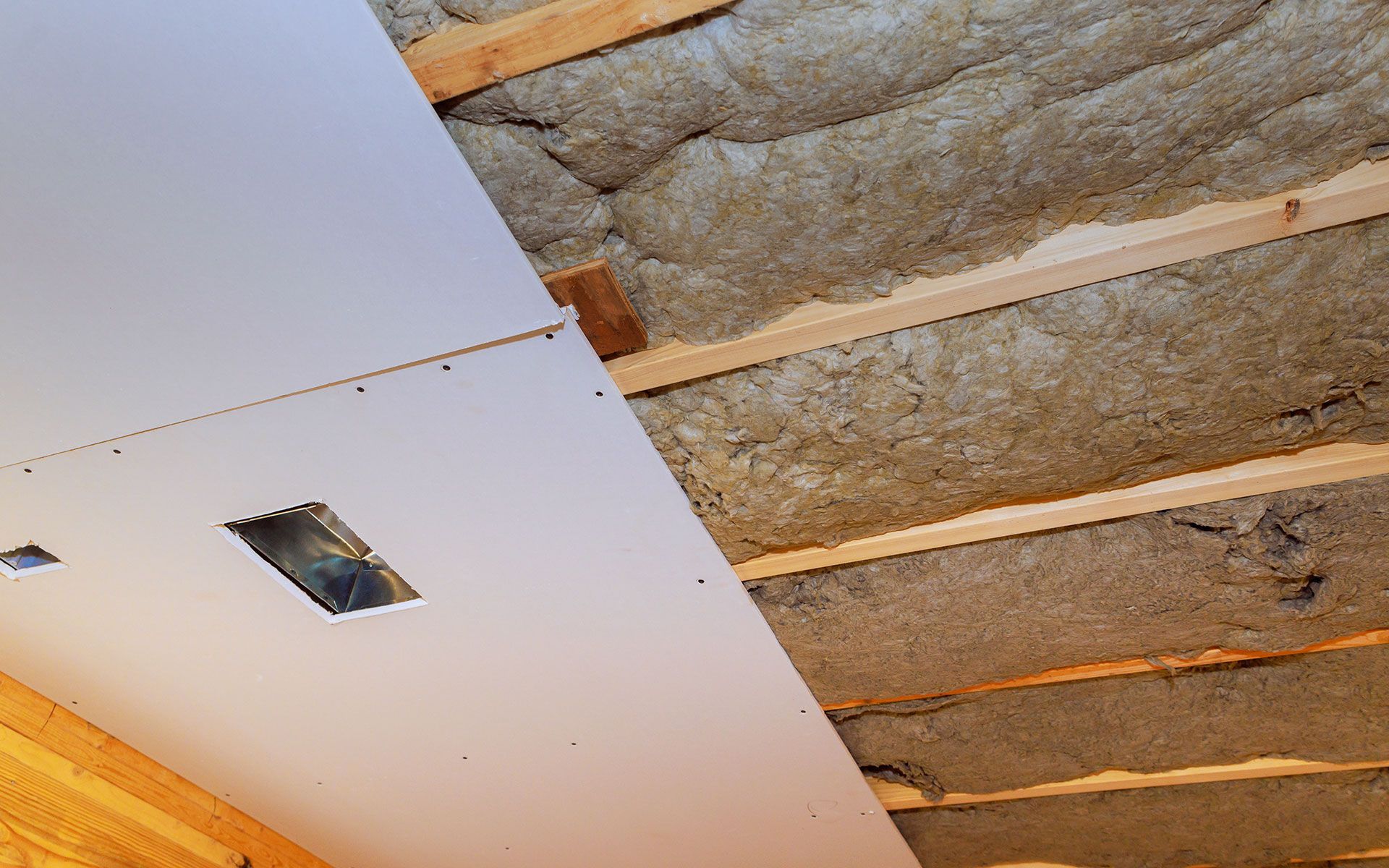 Ceiling under construction with drywall partially installed, revealing insulation and wooden beams.