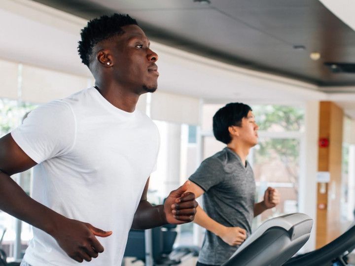 Two men are running on treadmills in a gym.