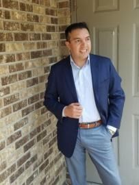 Man in a blue blazer and light jeans leaning against a brick wall in a doorway