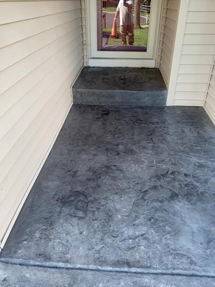 Concrete walkway leading to a front door with a small step and beige siding on both sides
