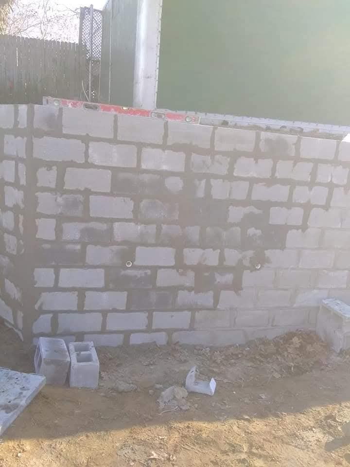 Partially built cinder block wall at a construction site, with debris and buckets on the ground.