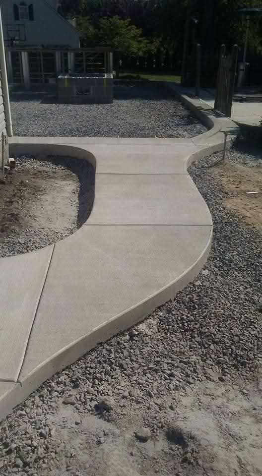 Curved concrete walkway through gravel leading to a porch in a shaded yard