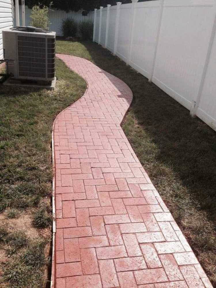 Curved red brick walkway beside a white fence and grass yard