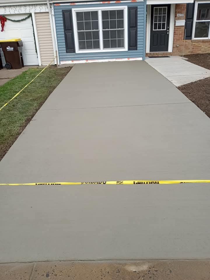 Freshly poured concrete driveway leading to a townhouse front entrance, with a yellow tape barrier across it