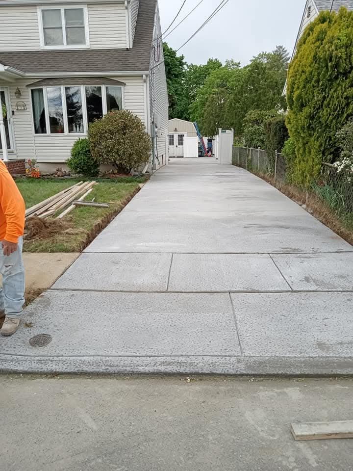 New concrete driveway beside a gray house, with a person in an orange shirt at the left edge.
