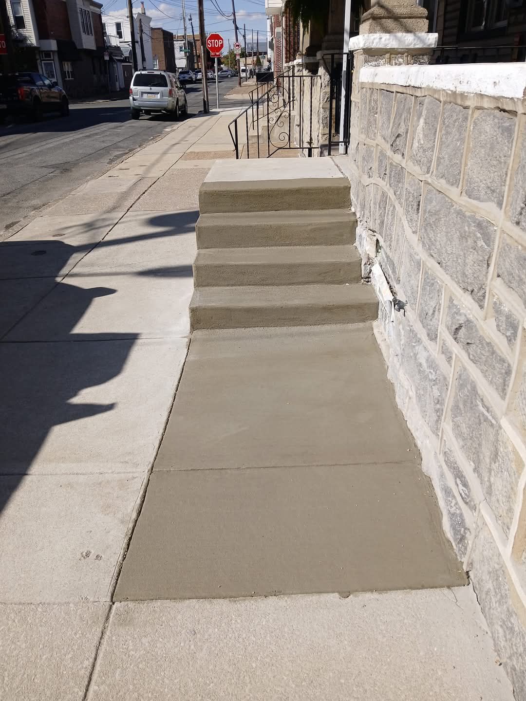 Concrete ramp with steps beside a stone wall on a city sidewalk