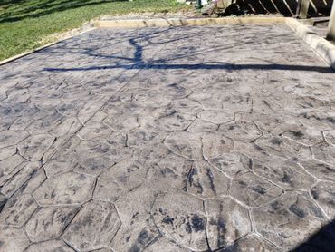 Stamped concrete patio with tree shadows and a grassy edge by a wooden fence