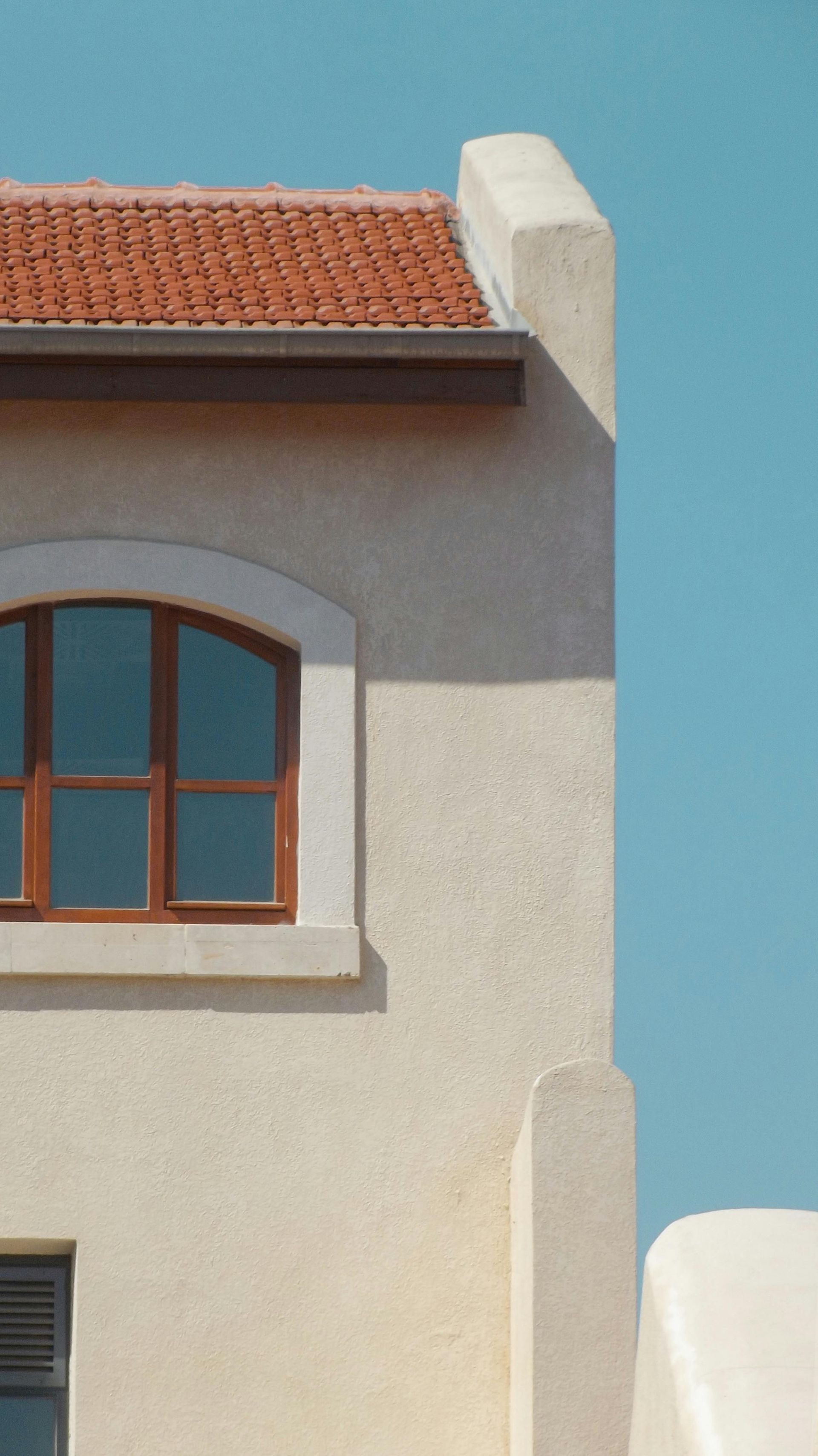 White stucco building with red tiled roof and arched window against a blue sky