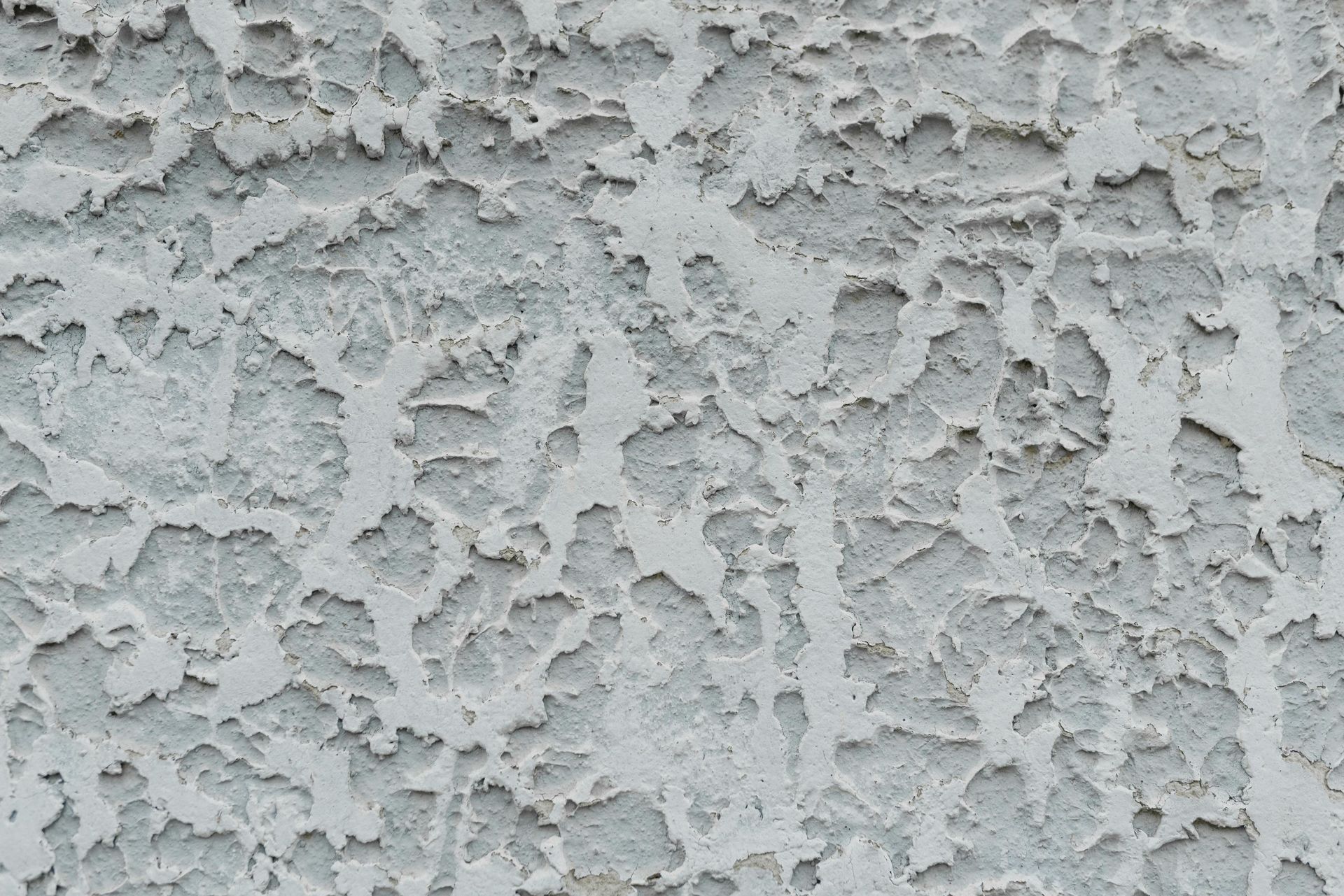 Close-up of rough, light gray stucco wall texture with chipped surface details