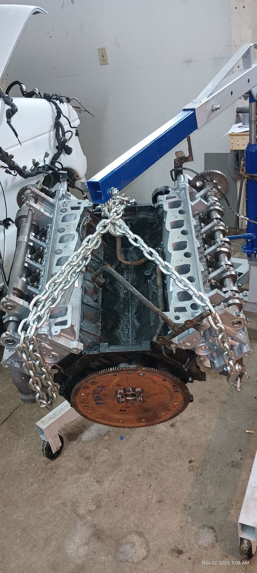 An engine block suspended by a chain and hoist in a garage setting.