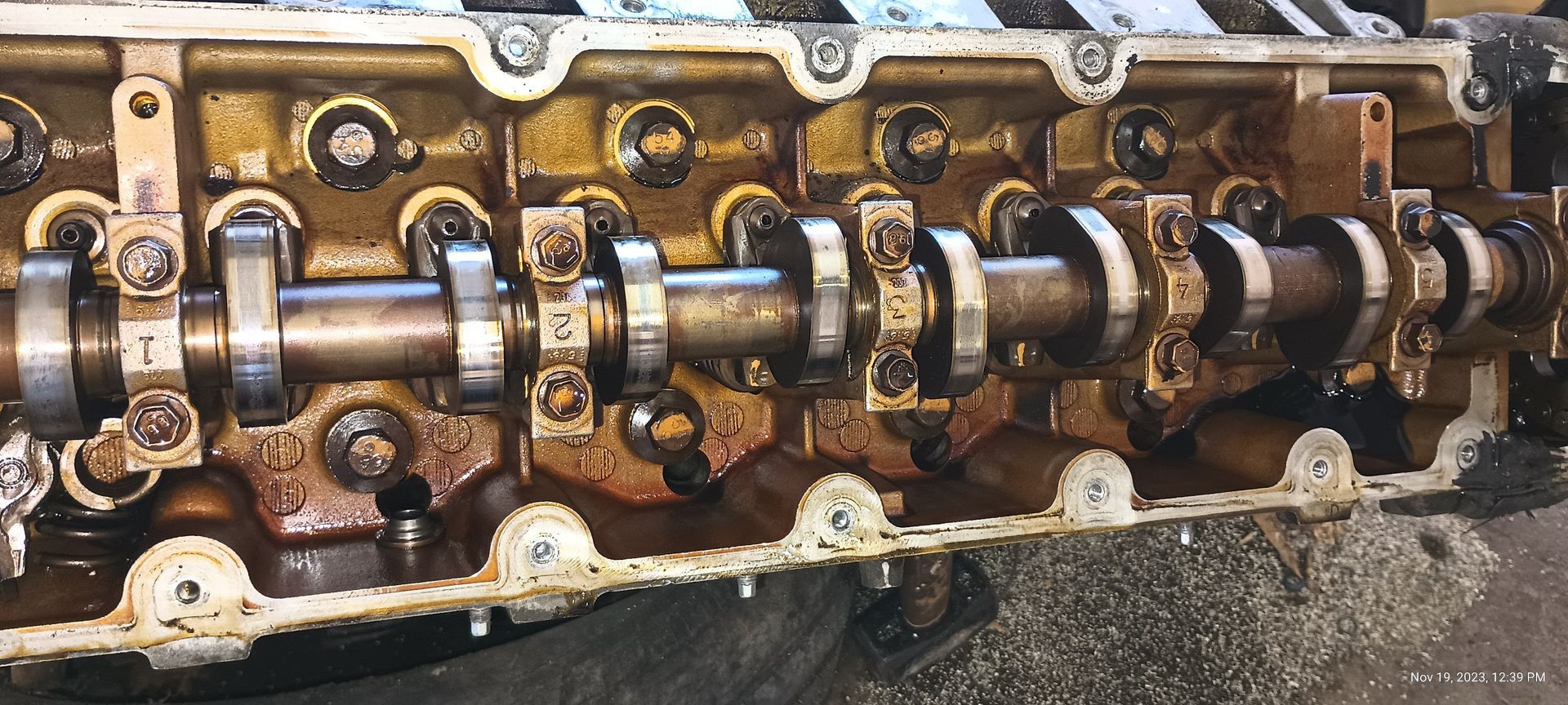 Engine cylinder head with visible camshafts and associated components, covered in oil.