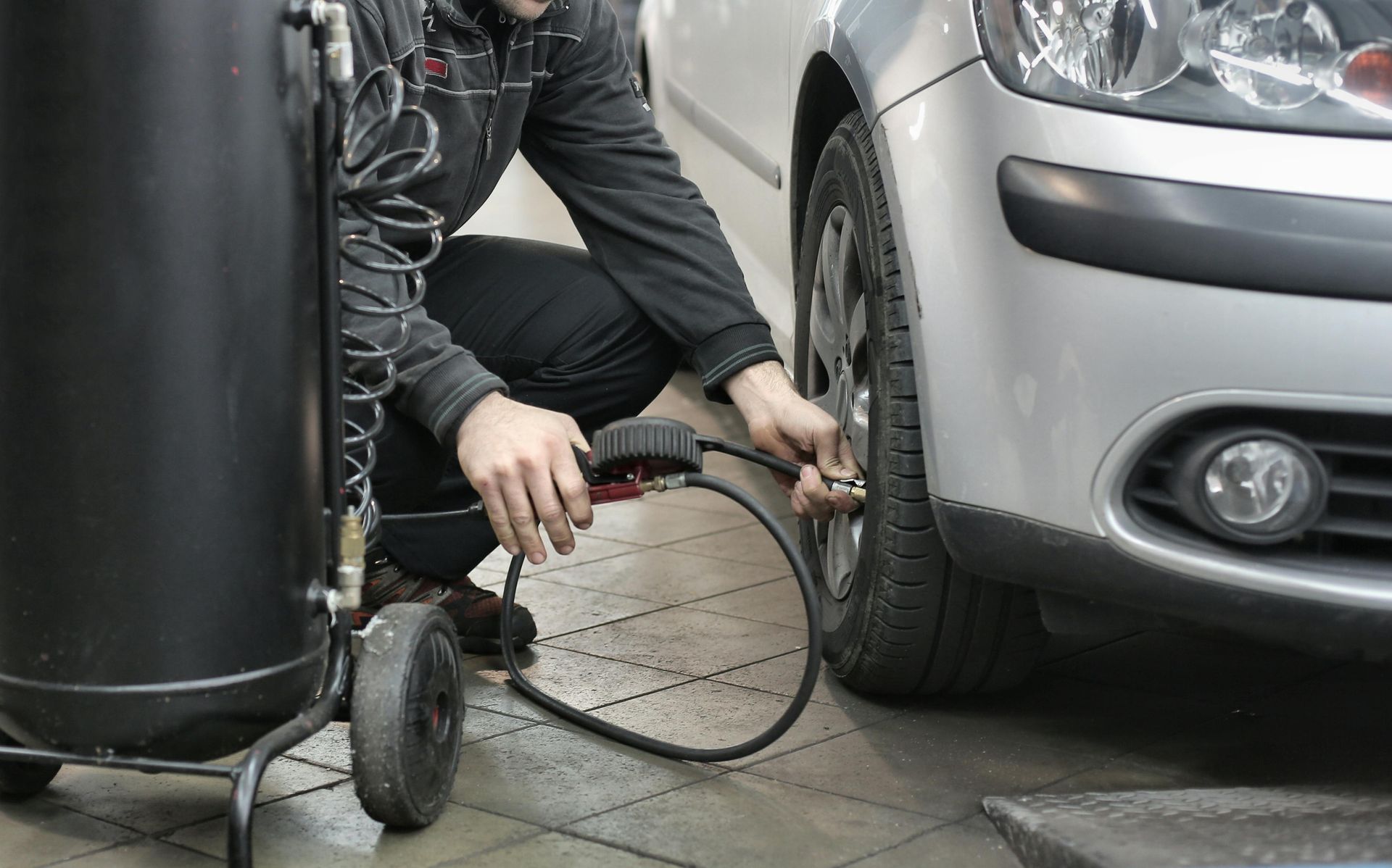 A person inflates a silver car tire with an air compressor in a garage.
