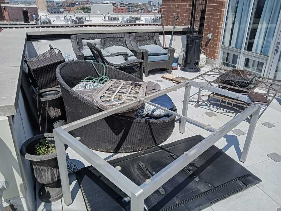 Rooftop patio with furniture including chairs, a table frame, and a heater; city view in background.