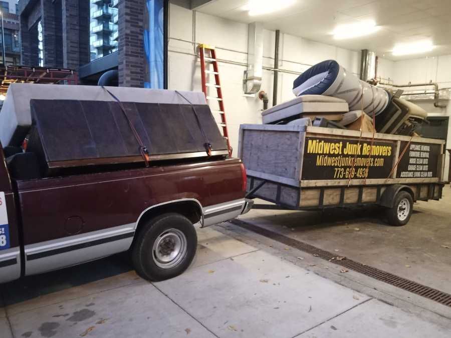 A burgundy pickup truck with a trailer loaded with furniture, ready for removal.