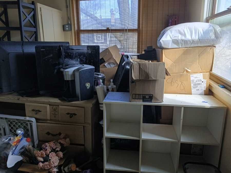 Cluttered room with old TVs, boxes, and storage units near a window.