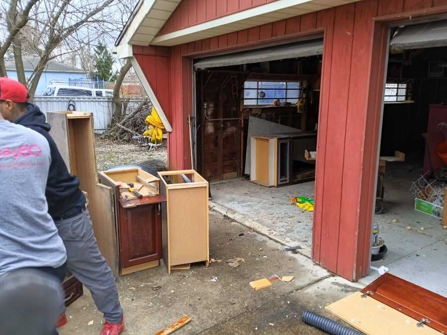 Two people moving furniture out of a red garage with open doors.