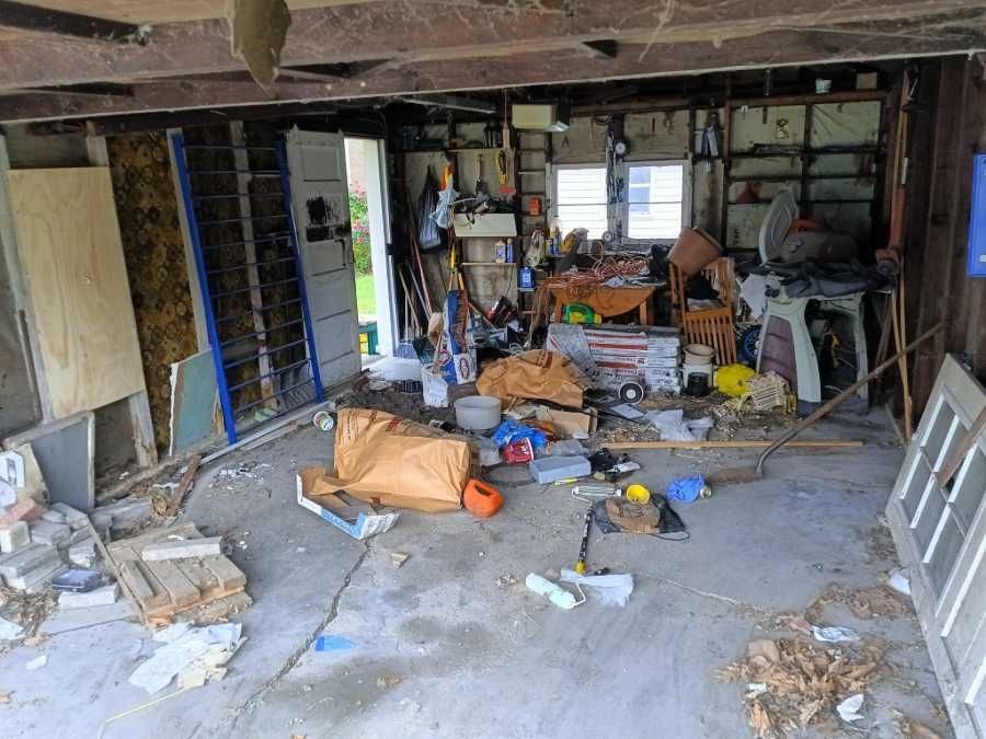 Messy garage interior; debris, tools, and clutter covering the floor and surfaces.