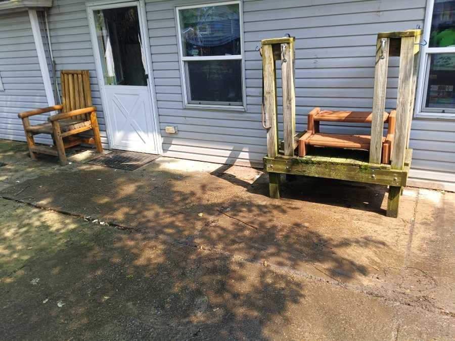 Wooden chair and steps by a back door on a concrete patio.