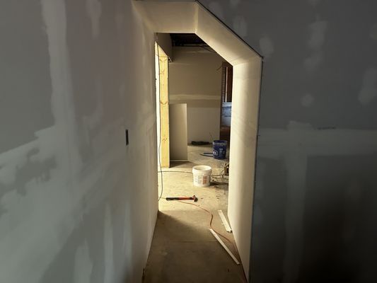 A hallway with a door and a bucket of paint on the floor.