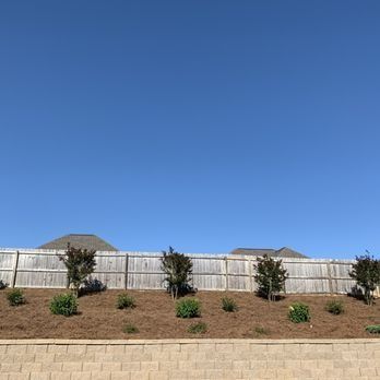 A wooden fence surrounds a lush green hillside with trees and bushes.