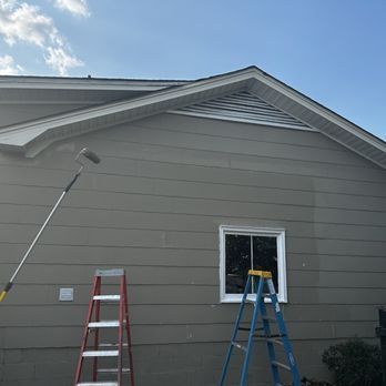 A person is painting the side of a house with a paint roller.